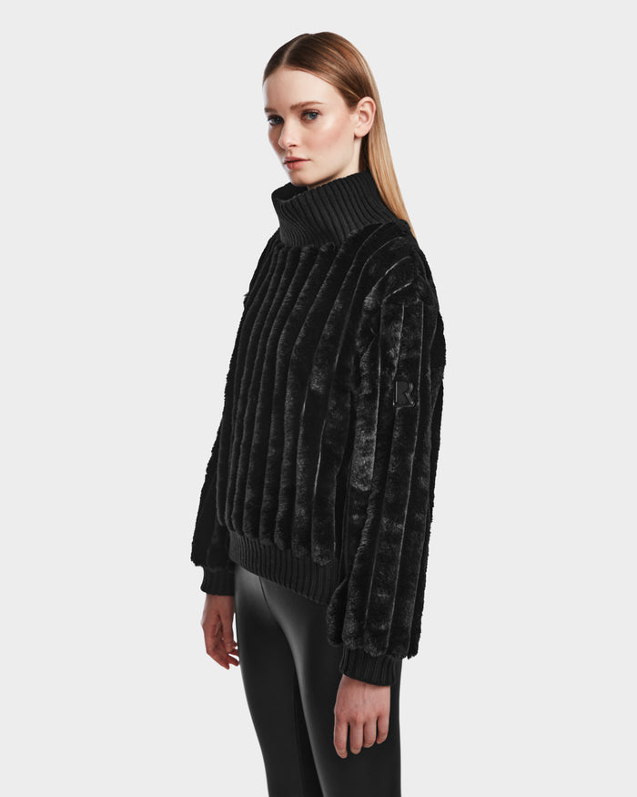 A woman with straight, light brown hair models the LAYLA - 8524610 Black turtleneck by Rudsak and shiny black pants, standing against a plain light background and facing slightly to the side with a neutral expression.