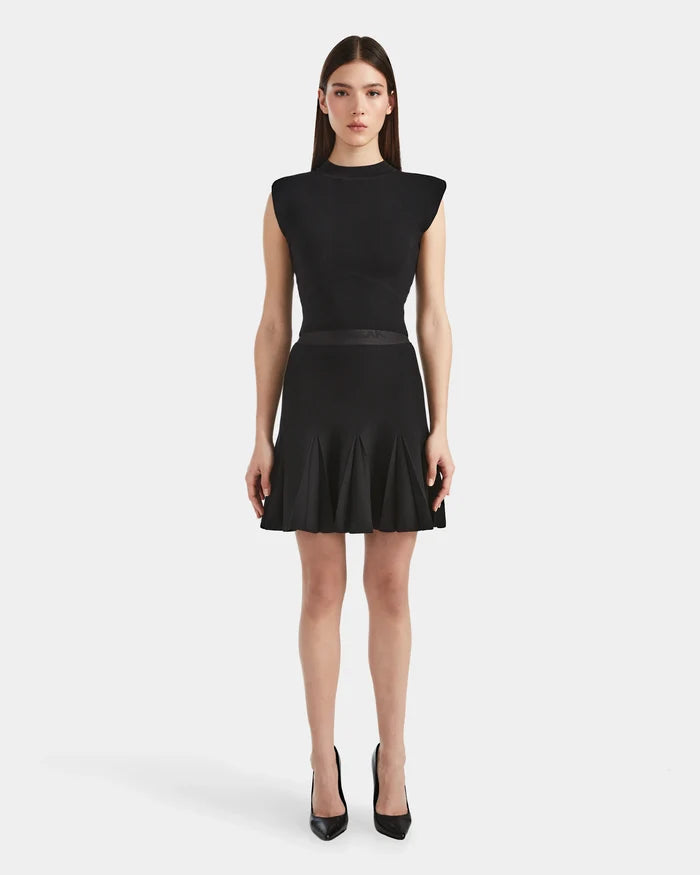 A woman stands facing forward, wearing Rudsaks LEA - 8524064 Black sleeveless dress with structured shoulders and a flared soft knit skirt, paired with black heels against a plain white background.