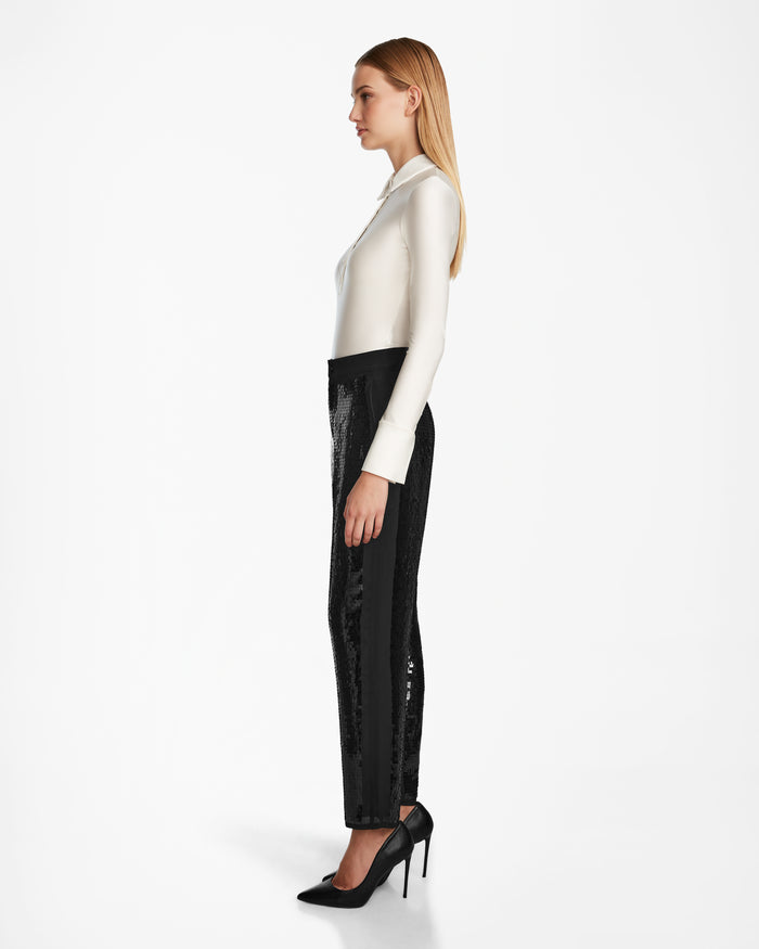 A woman with straight blonde hair, dressed in a white long-sleeve blouse and Rudsak LEAR - 8524553 Black pants, stands in profile against a plain white background.