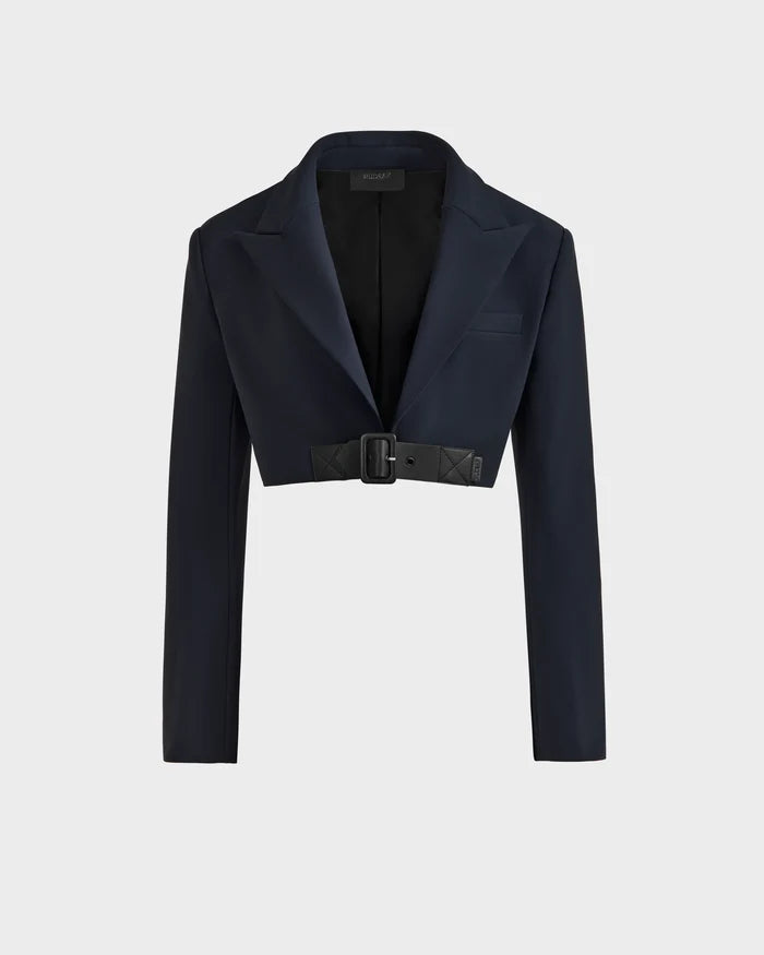 The Rudsak LEXI - 8525026 Black is a womens dark navy blue cropped blazer with long sleeves, wide lapels, and a black vegan leather belt with a rectangular buckle at the waist, shown on a plain light gray background.