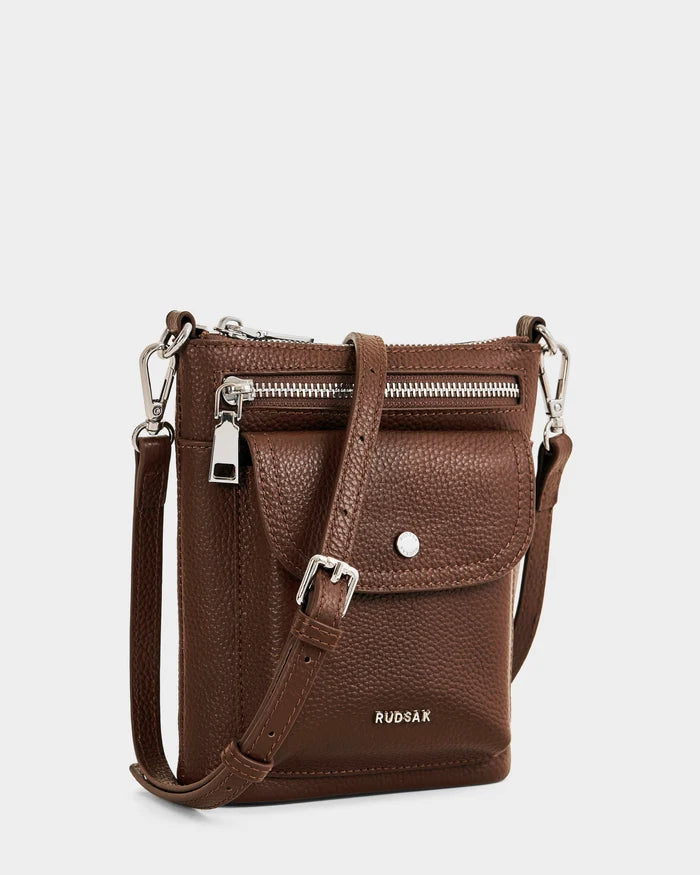 The LILA - L325513 Mocha by Rudsak is a small brown women's leather crossbody bag with a front zip pocket, buckle and snap-closure flap pocket, silver hardware, adjustable strap, and embossed Rudsak logo for a city-ready style.