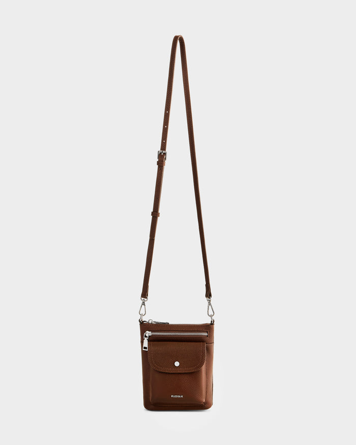 The Rudsak LILA - L325513 Mocha is a stylish women’s crossbody bag crafted in brown pebbled leather, featuring an adjustable strap, front flap pocket with snap button, zippered top closure, and a metallic logo—perfect for everyday use.