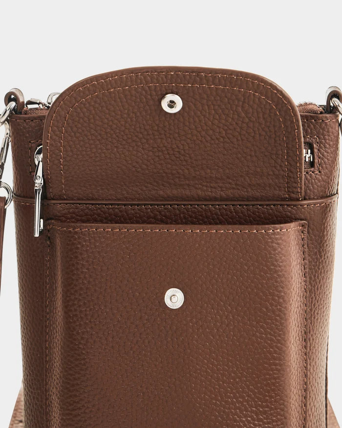 Close-up of the Rudsak LILA - L325513 Mocha bag in brown pebbled leather, with its front flap open to show a silver snap button, zippered compartment, structured pocket, and elegant silver hardware—perfect for the city.