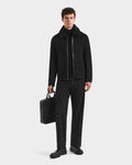 A man stands against a plain background wearing the Rudsak LINCOLN - 6125038 Black mens wool coat with a removable faux fur collar, paired with black clothes and shoes. He holds a black briefcase in his left hand, looking straight ahead.
