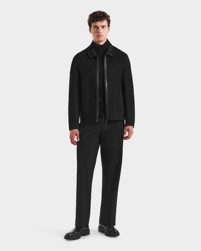 A man with short curly hair stands against a plain white background wearing the Rudsak LINCOLN - 6125038 Black jacket with removable faux fur collar, paired with a black turtleneck, pants, and shoes.