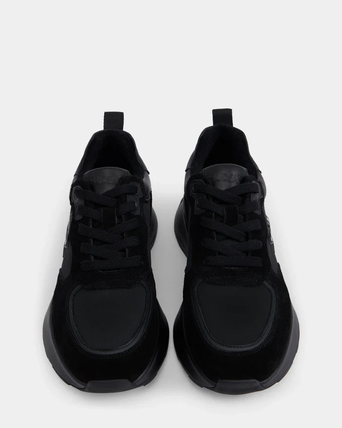 A pair of Rudsak LIONEL - 6225001 Black men’s lace-up sneakers with black laces, seen from above on a light gray background. They feature a modern design, subtle stitching, and a mix of suede and mesh textures.