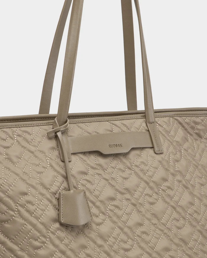 A close-up of the Rudsak LIVORNO - L325007 Almond bag shows beige stitching, twin shoulder straps, a small hanging tag, and the brand name on a leather detail at the top of this luxury carryall.