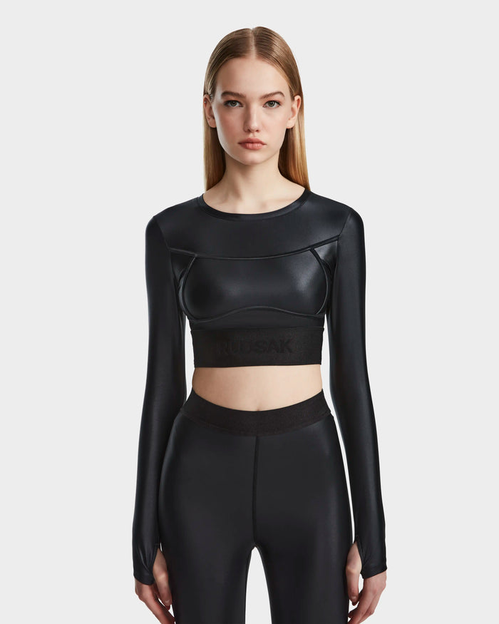 A young woman with straight, light brown hair wears the Rudsak LORA - 8524026 Black fitted technical top and matching high-waisted pants, standing against a plain light gray background.