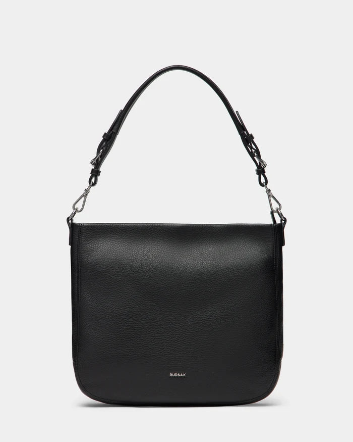 The Rudsak LUCYLE - 8325012 Black women’s leather hobo bag features a wide adjustable strap, silver hardware, a simple rectangular design, and discreet branding near the bottom center.