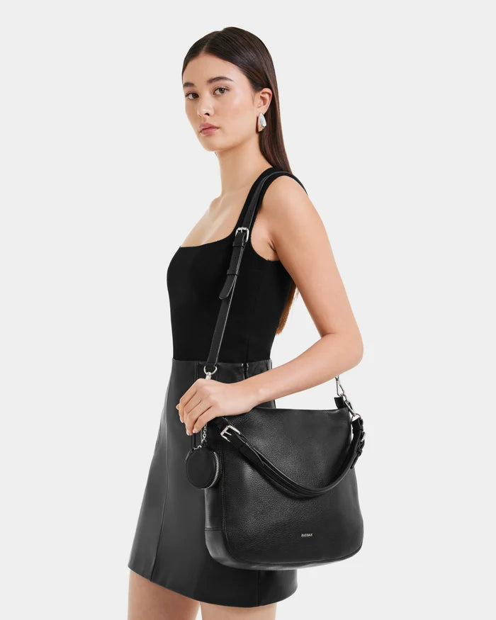 A woman in a black dress holds the Rudsak LUCYLE - 8325012 Black hobo bag, effortlessly showcasing her style with the chic accessory.
