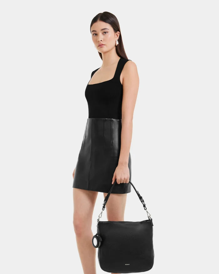 A woman in a black sleeveless top and leather skirt holds the Rudsak LUCYLE - 8325012 Black womens hobo bag with shoulder strap, standing against a plain light background.