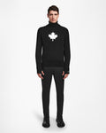 A person wears the Rudsak LUKAS - 6524543 Black mens knit turtleneck sweater with a white maple leaf design, paired with black pants and boots, perfect for après-ski style, facing forward against a plain white background.