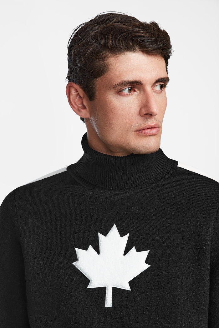 A man with short brown hair wears the Rudsak LUKAS - 6524543 Black men’s knit turtleneck sweater, featuring a bold white maple leaf emblem, looking slightly left against a plain white background—ideal for après-ski style.