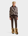 A person faces forward wearing Rudsak's LYDIA - 8525687 Espresso sweater, brown leggings, a furry hat, and tan fur boots—showcasing cozy après-ski style against a plain light background.