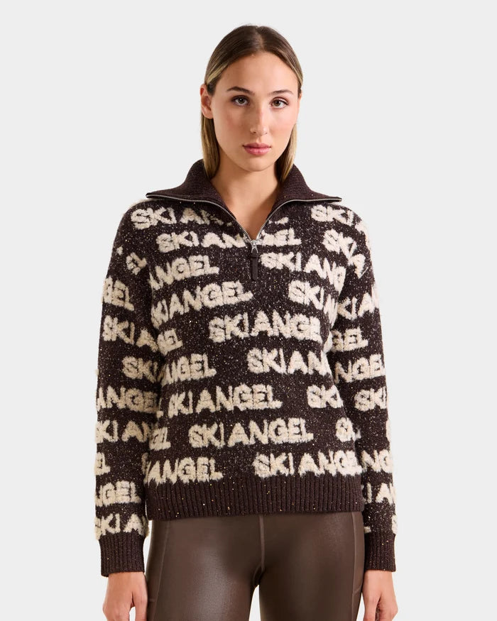 A woman with straight, light brown hair models the Rudsak LYDIA - 8525687 Espresso women’s ski pullover featuring bold white SKI ANGEL text, styled with shiny brown leggings against a plain white background for an après-ski vibe.