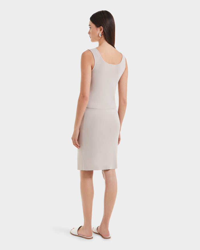 A woman with straight brown hair stands facing away, wearing the Rudsak MARIE - L525007 Cream sleeveless dress featuring a scoop neckline and above-the-knee length, paired with white flat sandals against a plain white background.