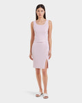 A woman stands facing forward in Rudsak’s MARIE - L525007 Light Pink sleeveless knit top and matching knee-length skirt with side slit, paired with white slide sandals against a plain white background—ideal for the modern wardrobe.