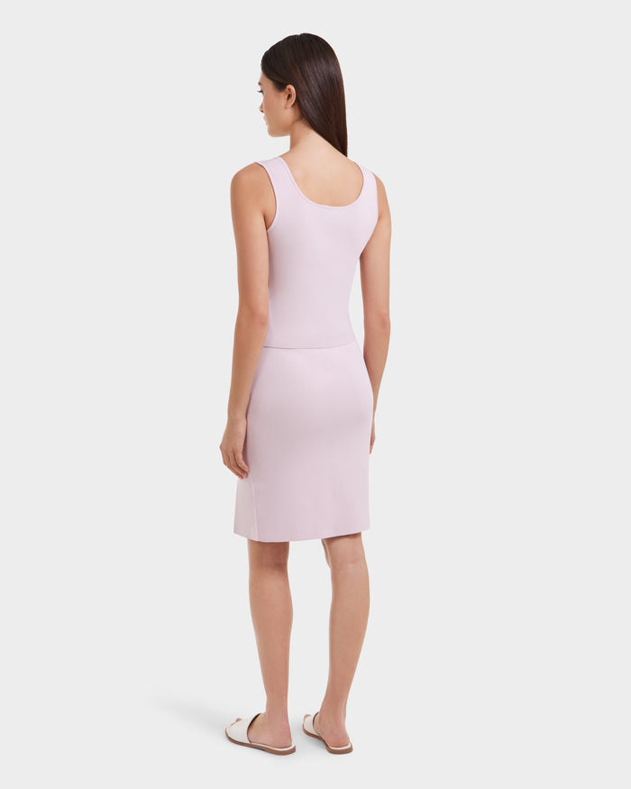 A woman with straight dark hair faces away, wearing the MARIE - L525007 Light Pink sleeveless top by Rudsak and white sandals, creating a modern look against a plain white background.