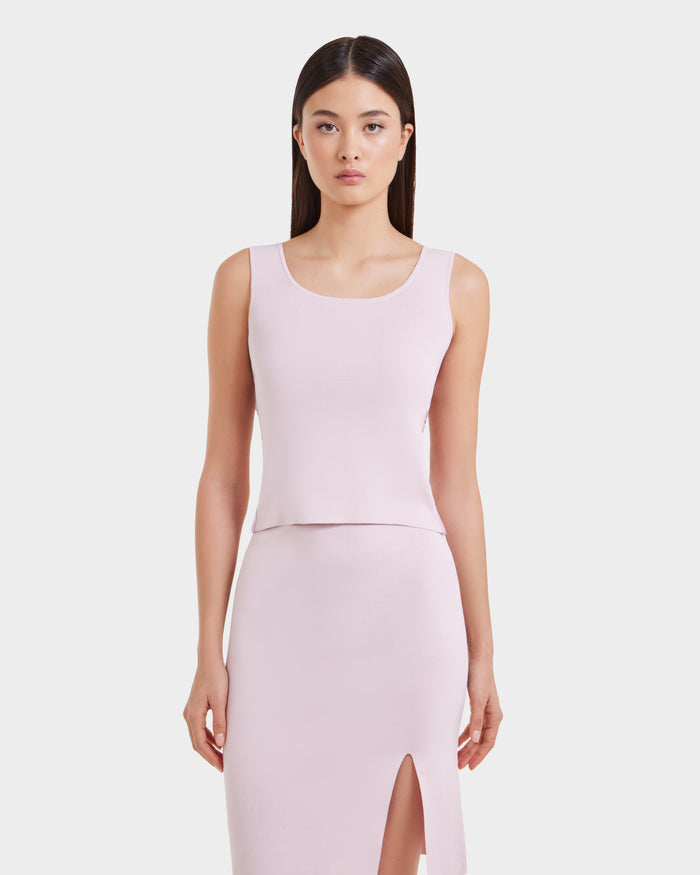 A woman with straight dark hair models the Rudsak MARIE - L525007 light pink sleeveless scoop-neck top and matching front-slit skirt, standing against a plain white background.