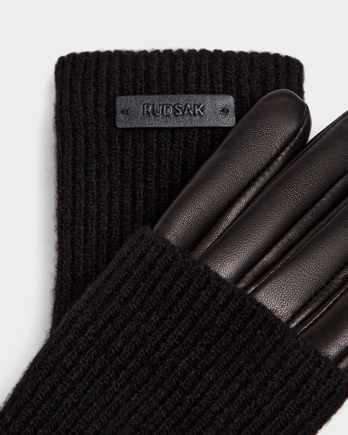 Close-up of Rudsak's MARINE - 8424516 Black/Black women's glove, featuring black knit wool, smooth black leather fingers, a ribbed cuff, and a Rudsak patch label—an elegant fall accessory.