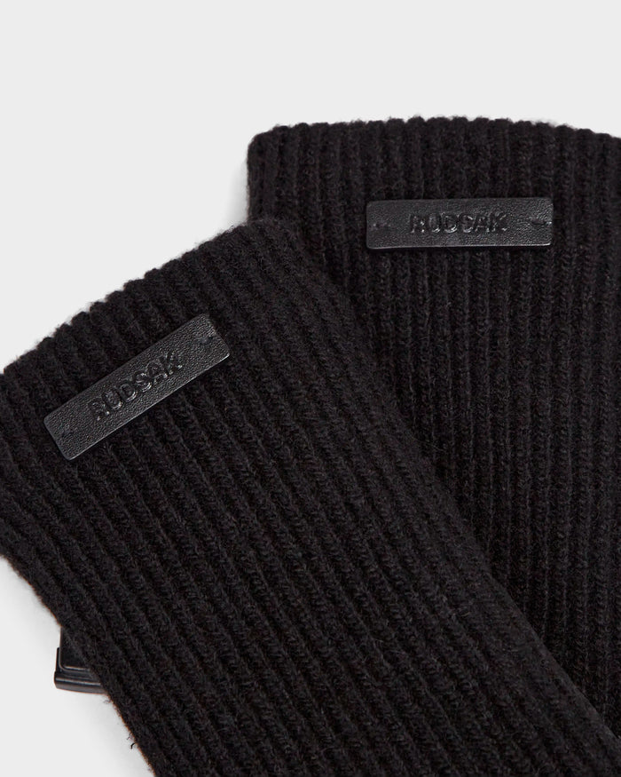 Close-up of MARINE - 8424516 Black/Black ribbed knit wool gloves by Rudsak, featuring rectangular black labels with raised RUDSAK lettering, partially overlapping on a white background—perfect chic fall accessories.