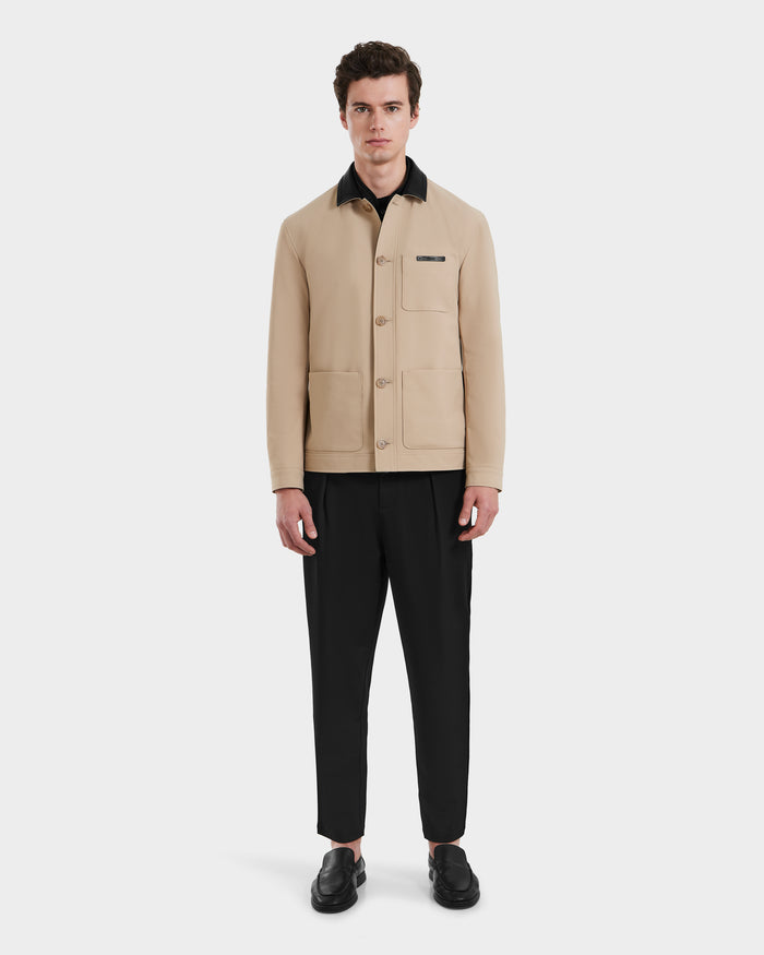 A man stands facing forward against a plain white background, wearing the Rudsak MATTHEW - 6125004 Almond blazer-style shirt jacket with large front pockets, paired with black pants and black shoes.