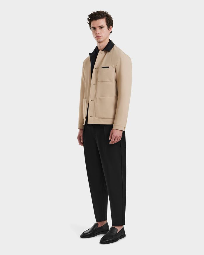A man stands against a plain background wearing the Rudsak MATTHEW - 6125004 Almond blazer-style shirt jacket over a black shirt, black loose-fitting trousers, and black loafers.