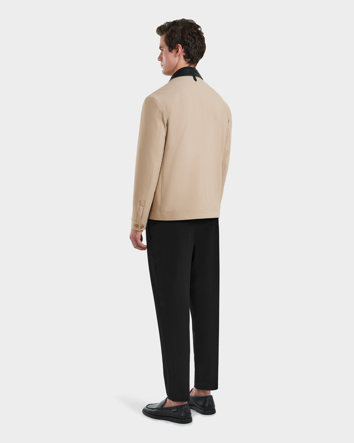 A man stands facing away, wearing the Rudsak MATTHEW - 6125004 Almond blazer-style shirt jacket with a black collar, black trousers, and black loafers against a plain white background.