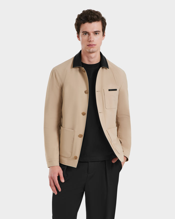 A man wears the Rudsak MATTHEW - 6125004 Almond blazer-style shirt jacket with a black collar, black shirt, and black pants, standing with one hand in his pocket against a plain white background.