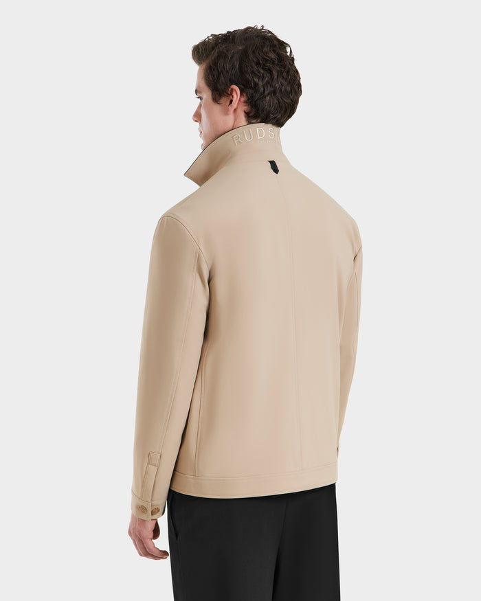 A man faces away, wearing Rudsaks MATTHEW - 6125004 Almond blazer-style shirt jacket with a high embroidered collar and black pants, set against a plain white background.