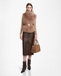 A woman poses against a white background wearing the Rudsak MAULIN - 8524611 Camel faux fur vest with a wide belt, styled with a brown vegan leather skirt, ankle boots, and a tan handbag.