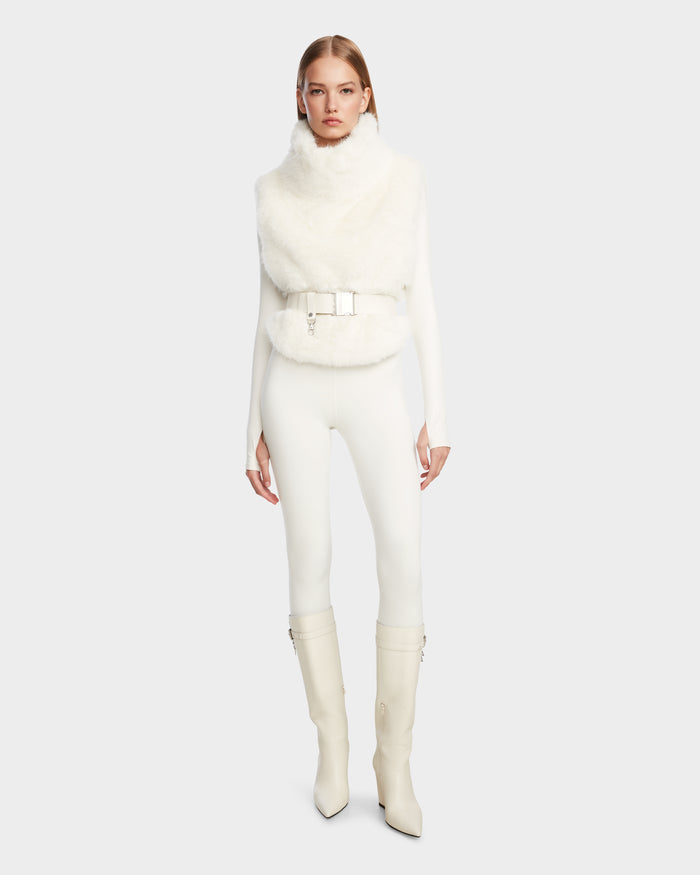A woman stands facing forward against a plain light background, wearing the Rudsak MAULIN - 8524611 Iceland sleeveless white faux fur belted vest over a white pullover, fitted pants, and knee-high heeled boots.