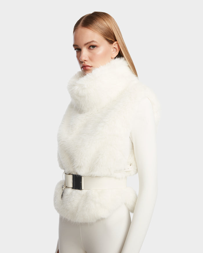 A woman with straight blonde hair models the Rudsak MAULIN - 8524611 Iceland sleeveless white faux fur vest with a high rolled collar and wide vegan leather belt, posing against a plain light background facing slightly to the side.