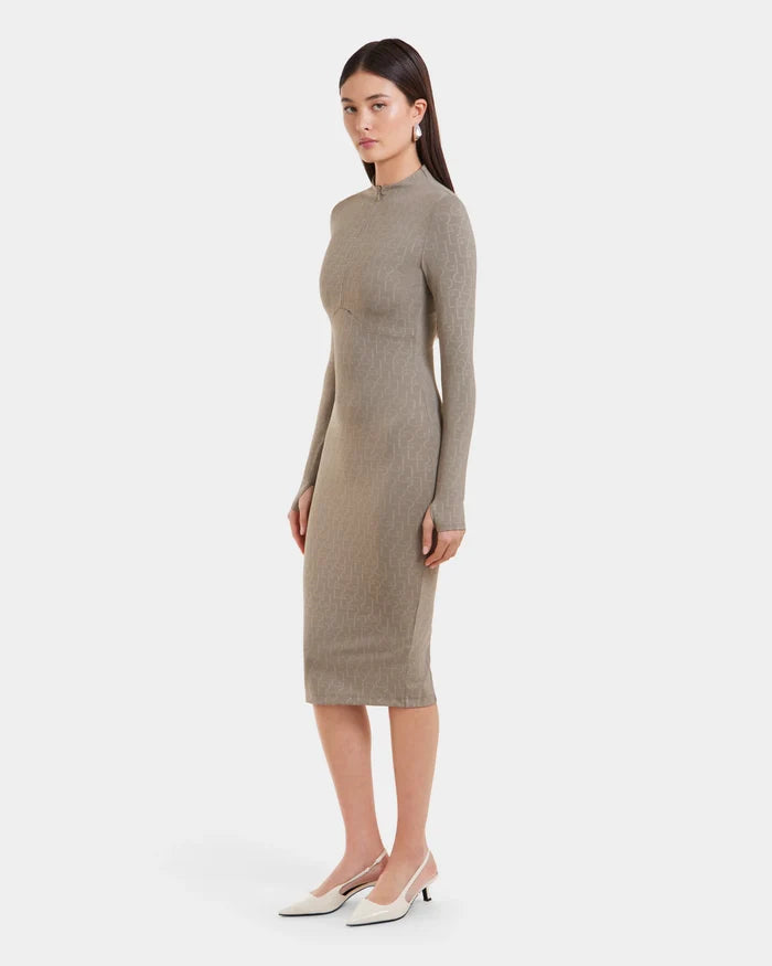 A woman with straight dark hair and a neutral expression stands on a white background wearing the Rudsak MAYLIN - 8523504 Cement Pattern long fitted dress, styled with statement earrings and white heeled slingback shoes.