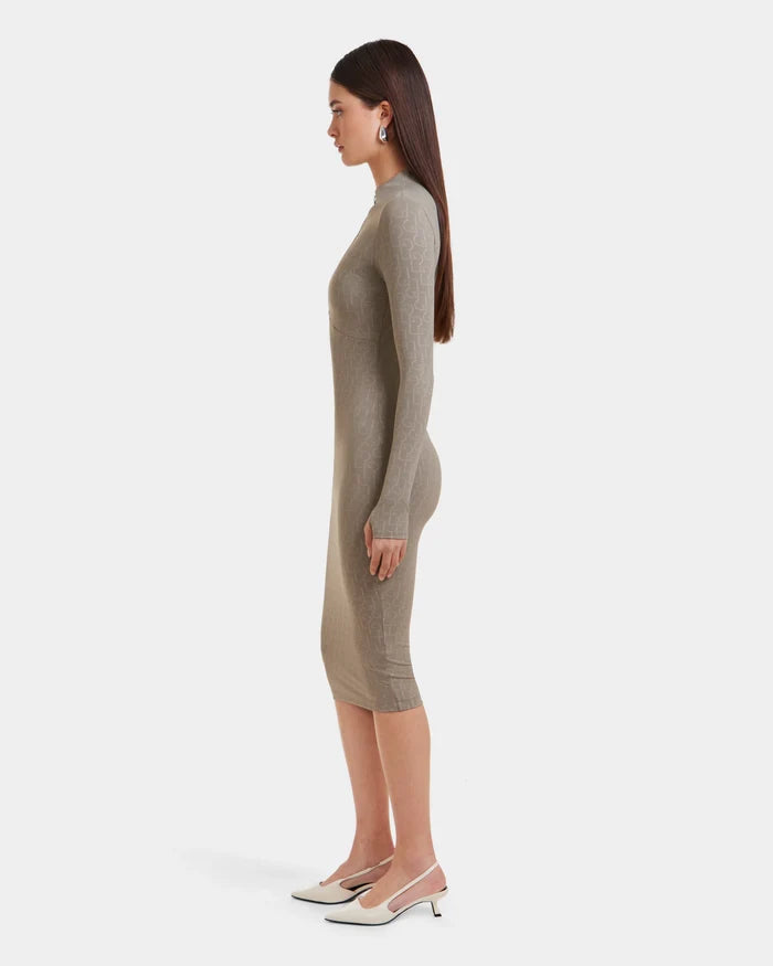 A woman with long brown hair stands in profile, wearing the Rudsak MAYLIN - 8523504 Cement Pattern women’s fitted dress and white slingback heels against a plain white background.