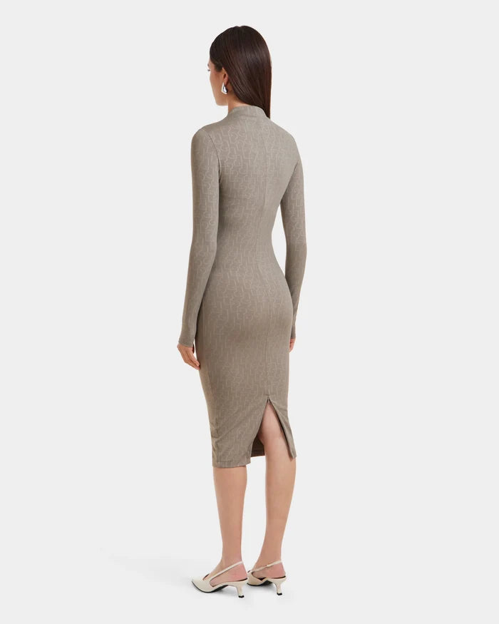 A woman with straight brown hair, seen from behind against a white background, wears the Rudsak MAYLIN - 8523504 Cement Pattern long fitted dress in light brown stretch fabric with subtle monogram, long sleeves, back slit, and white low-heeled shoes.