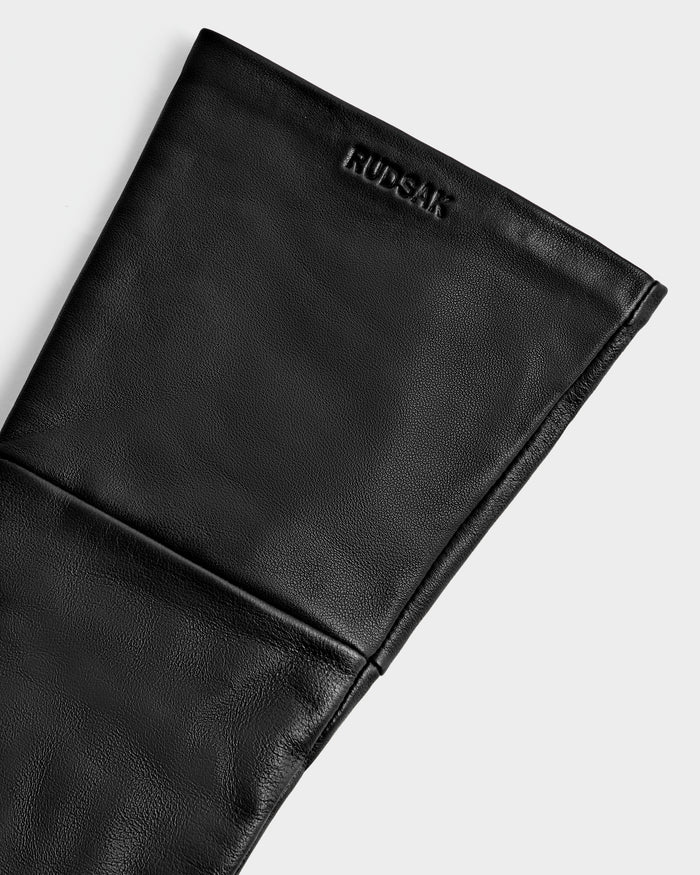 Close-up of the MEGAN - 8425541 Black women's accessory by Rudsak, made of folded black leather and embossed with the Rudsak logo near the top, displayed on a plain light background.