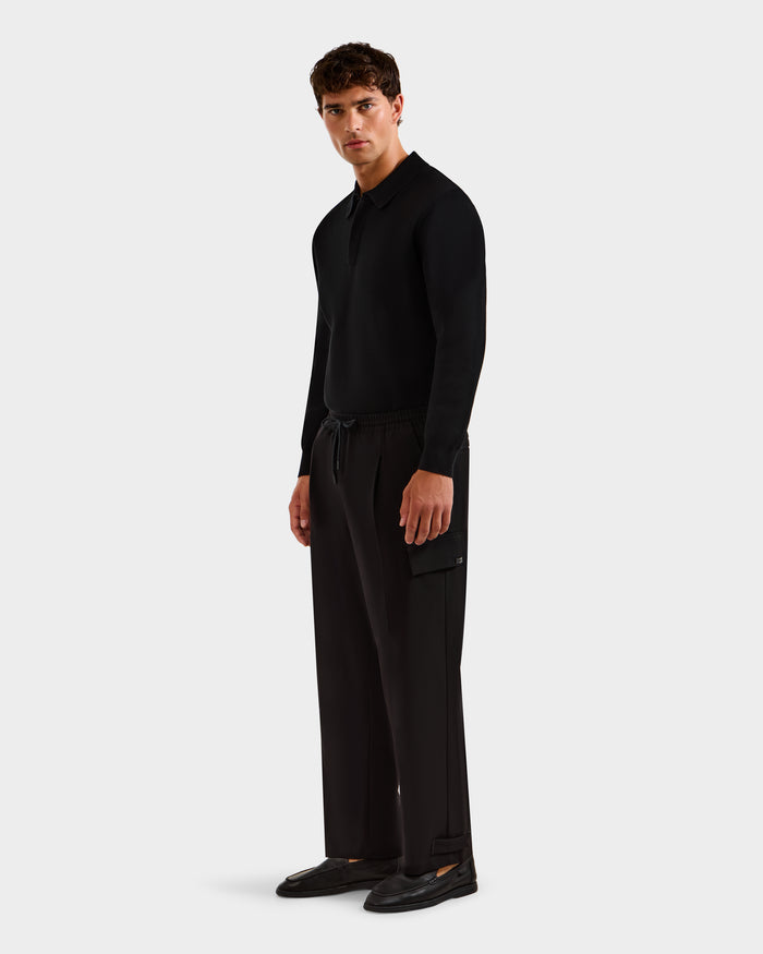 A man stands against a plain background wearing the MIKEY - 6525597 Black long-sleeve shirt by Rudsak, premium men’s trousers with a side pocket, and black shoes, looking slightly to the side with a neutral expression.