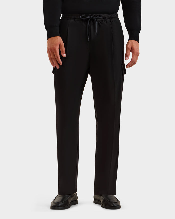 A person wears Rudsak’s MIKEY - 6525597 Black men’s trousers with a relaxed fit and side pockets, styled with a black long-sleeve shirt and shoes, standing against a plain white background.