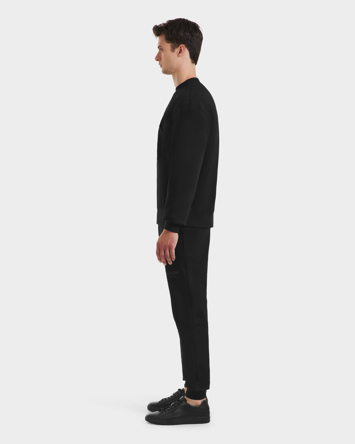 A man in profile faces left, wearing the Rudsak MILOS - 6525646 Black men’s premium sweatshirt and black pants with black sneakers, set against a plain white background.