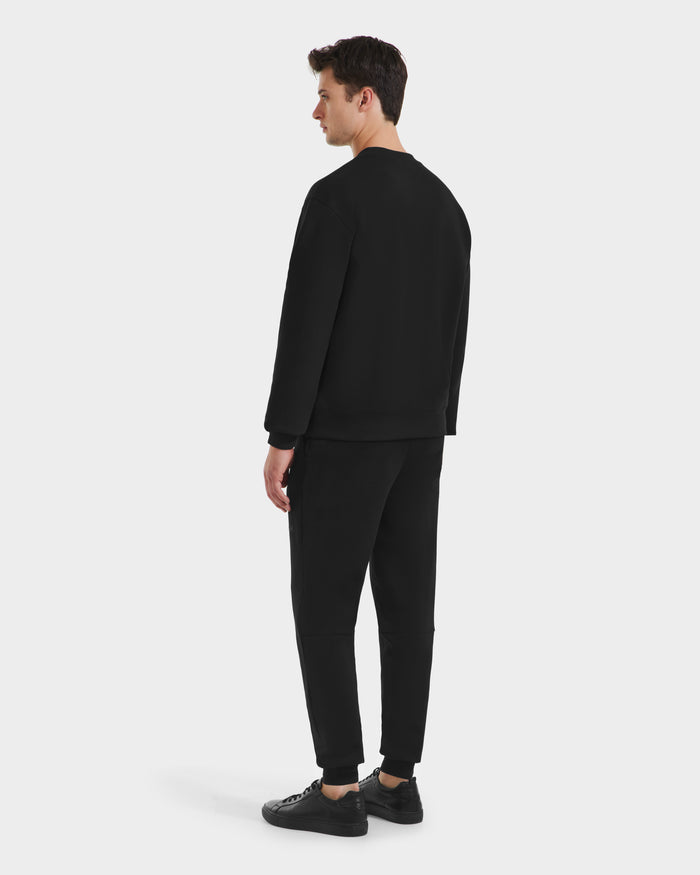 A man faces away, wearing the Rudsak MILOS - 6525646 Black mens premium sweatshirt with matching black pants and sneakers, set against a plain white background.