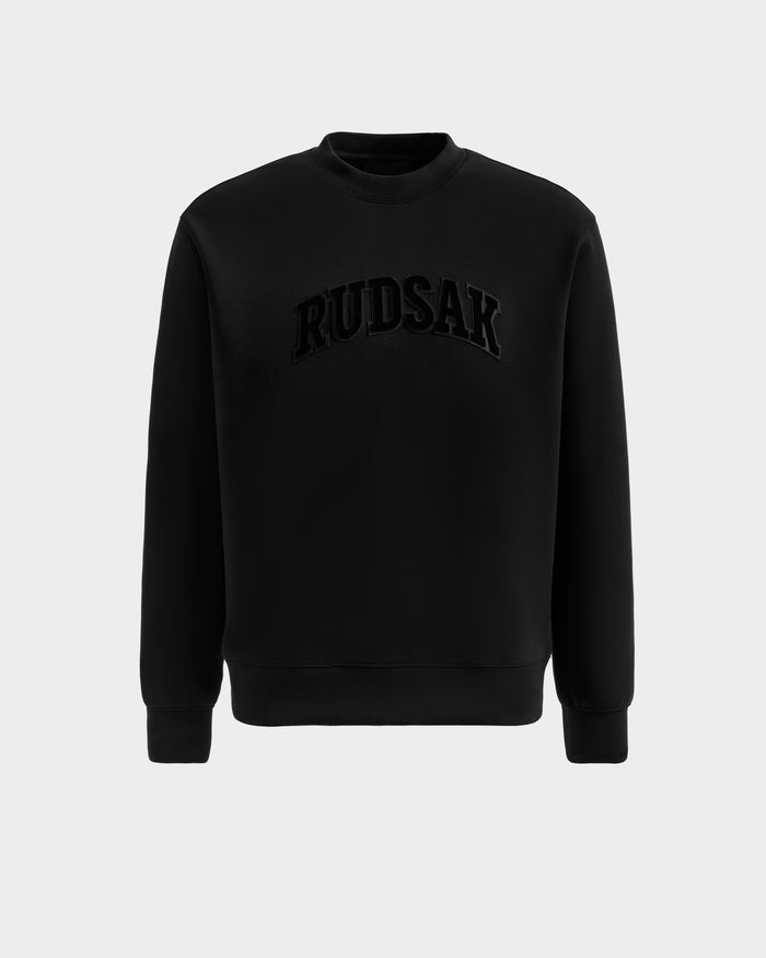 The Rudsak MILOS - 6525646 Black is a men's premium crewneck sweatshirt with long sleeves, made from a soft cotton blend and featuring bold raised RUDSAK lettering across the chest, shown against a plain light grey background.