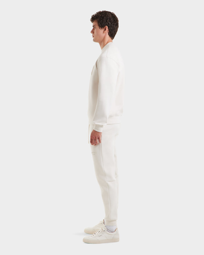 A man in profile against a plain background wears a minimalist all-white outfit, featuring the Rudsak MILOS - 6525646 Vanilla mens crewneck sweatshirt, jogger pants, and crisp white sneakers.