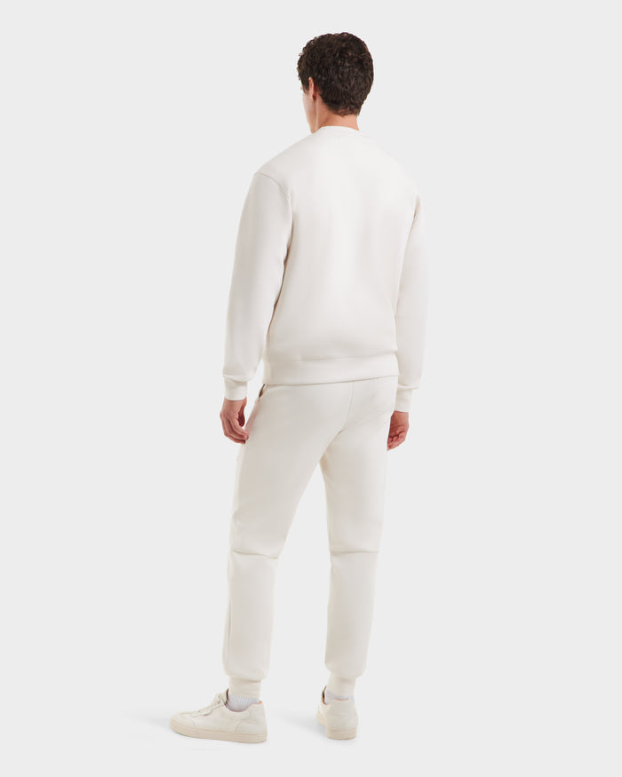 A person stands facing away, wearing the Rudsak MILOS - 6525646 Vanilla mens crewneck sweatshirt and sweatpants in a premium cotton blend, paired with white sneakers against a plain light background for a clean minimalist look.