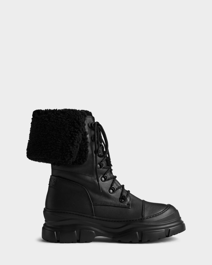 The MODENA - 8225024 Black boot by Rudsak features black leather, a chunky sole, and a folded faux shearling cuff—perfect winter boots for stylish comfort, shown in profile against a plain light background.