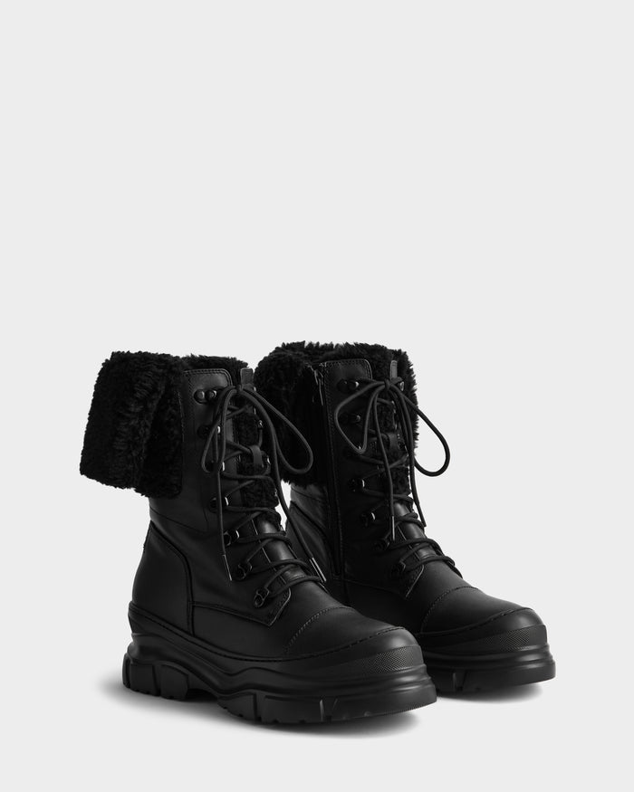 The Rudsak MODENA - 8225024 Black boots feature black leather, chunky soles, and folded-down faux shearling collars, shown against a light gray background.