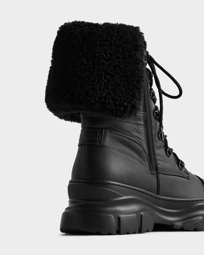 Close-up of Rudsak’s MODENA - 8225024 Black boot featuring black leather, a chunky sole, side zipper, and thick faux shearling cuff—ideal winter footwear—set against a plain white background.