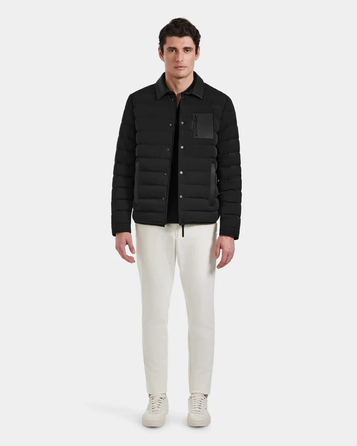 A man faces forward wearing the Rudsak NICHOLAS - 6125040 Black RDS-certified down quilted shirt jacket over a black shirt, white pants, and white sneakers against a plain light gray background.