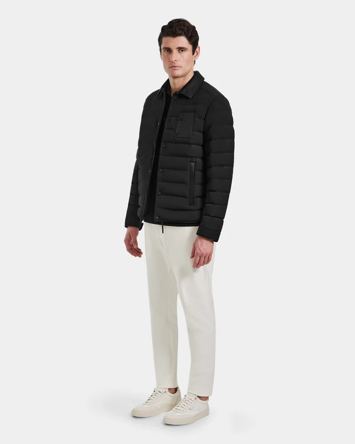 A man faces forward wearing the Rudsak NICHOLAS - 6125040 Black puffer jacket, off-white pants, and white sneakers—showcasing a mens wardrobe essential against a plain light gray background.
