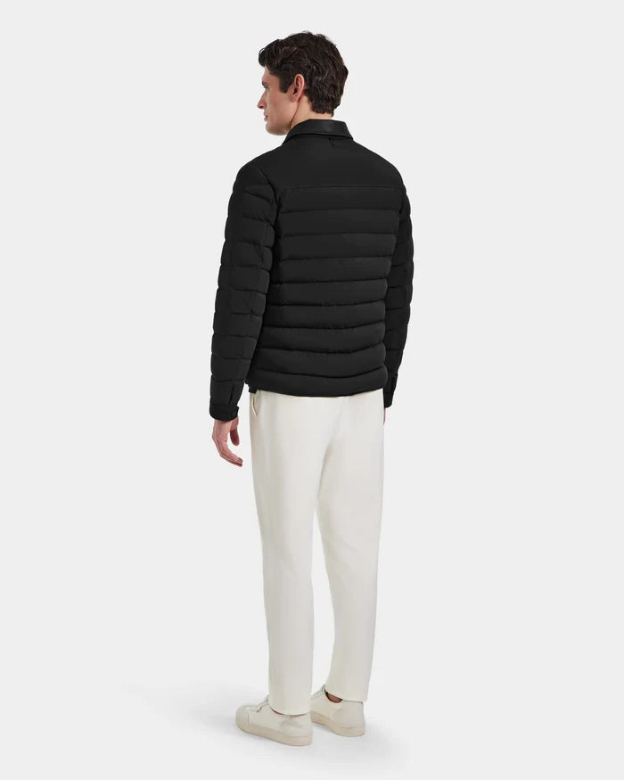 A man stands facing away in the Rudsak NICHOLAS - 6125040 Black quilted shirt jacket with RDS-certified down, paired with white pants and sneakers against a plain light background.
